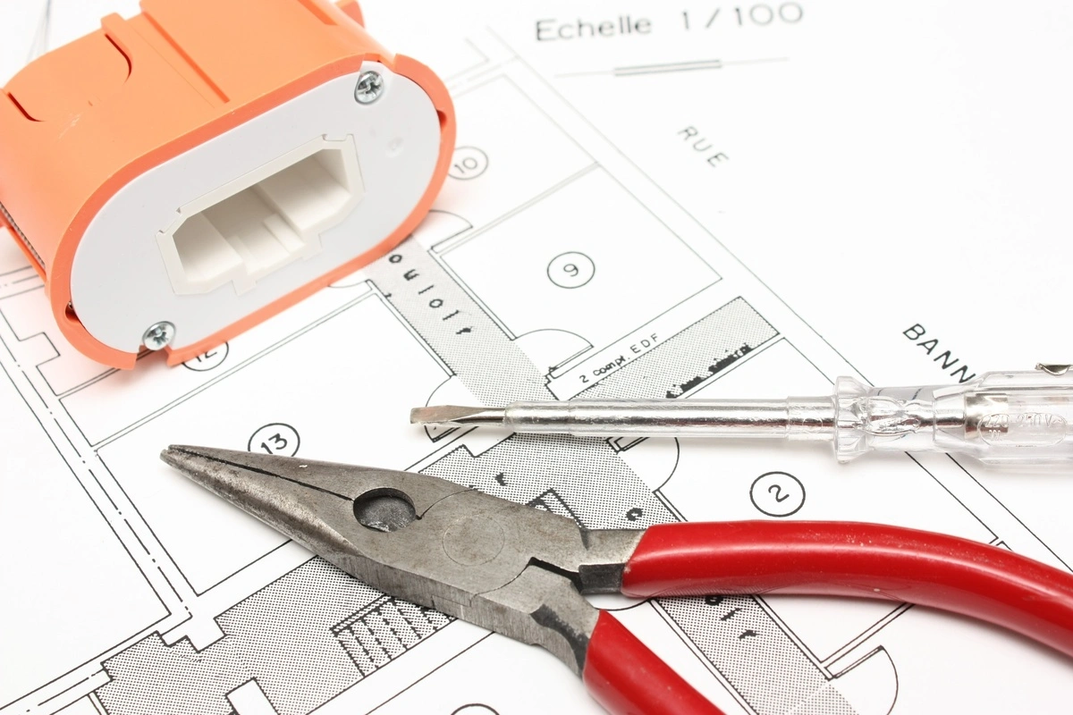outils d’électricien, plan technique et prise murale prêts pour une intervention de dépannage électrique dans un bâtiment