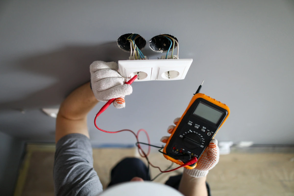 électricien en train de tester une prise électrique lors d'une installation intérieure, utilisant un multimètre pour vérifier la tension