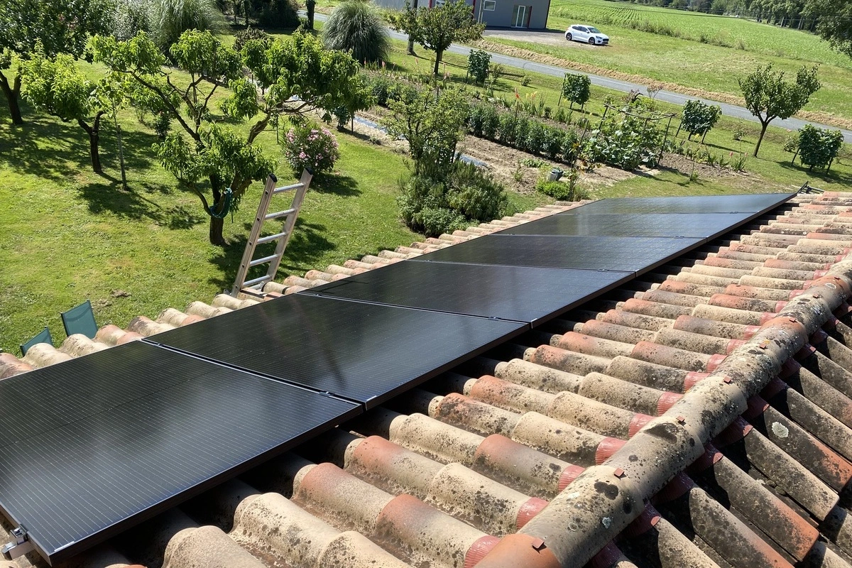 installation de panneaux photovoltaïques sur un toit de tuiles anciennes, vue depuis le toit avec un jardin en arrière-plan