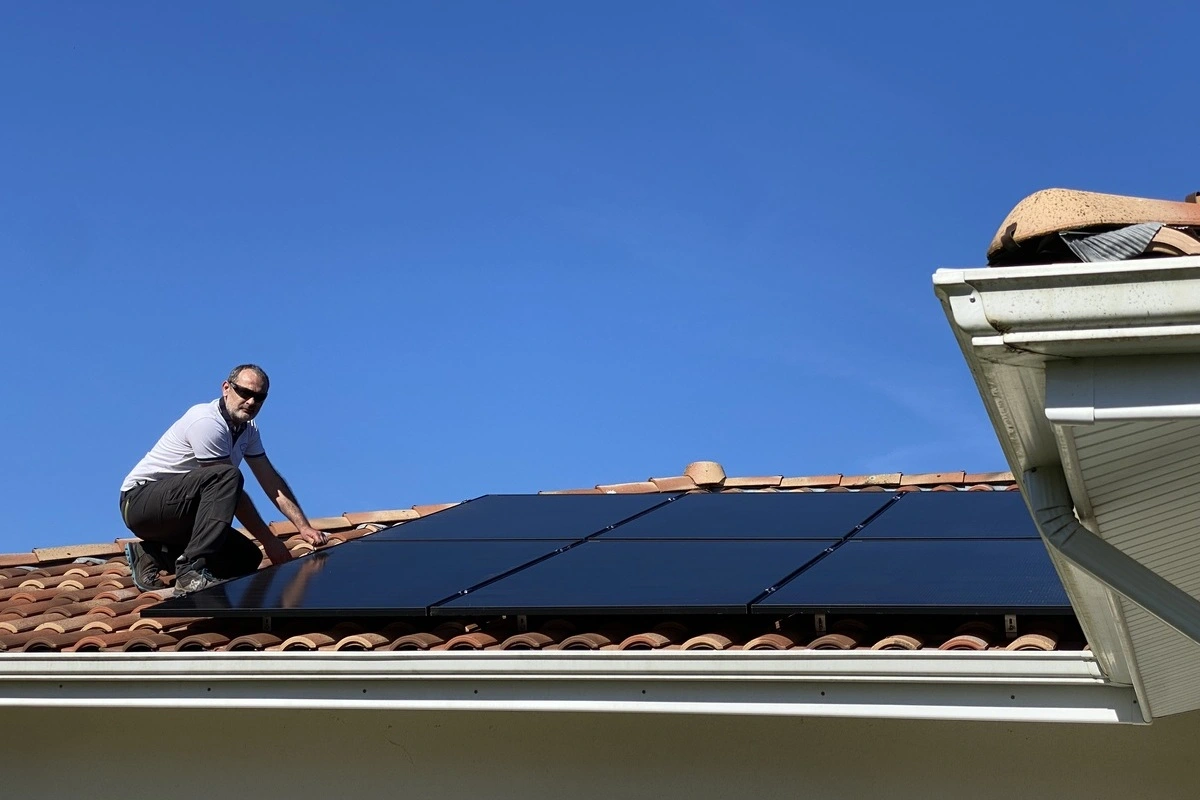 installateur de panneaux photovoltaïques terminant l’installation d’un système solaire sur un toit, ciel bleu dégagé